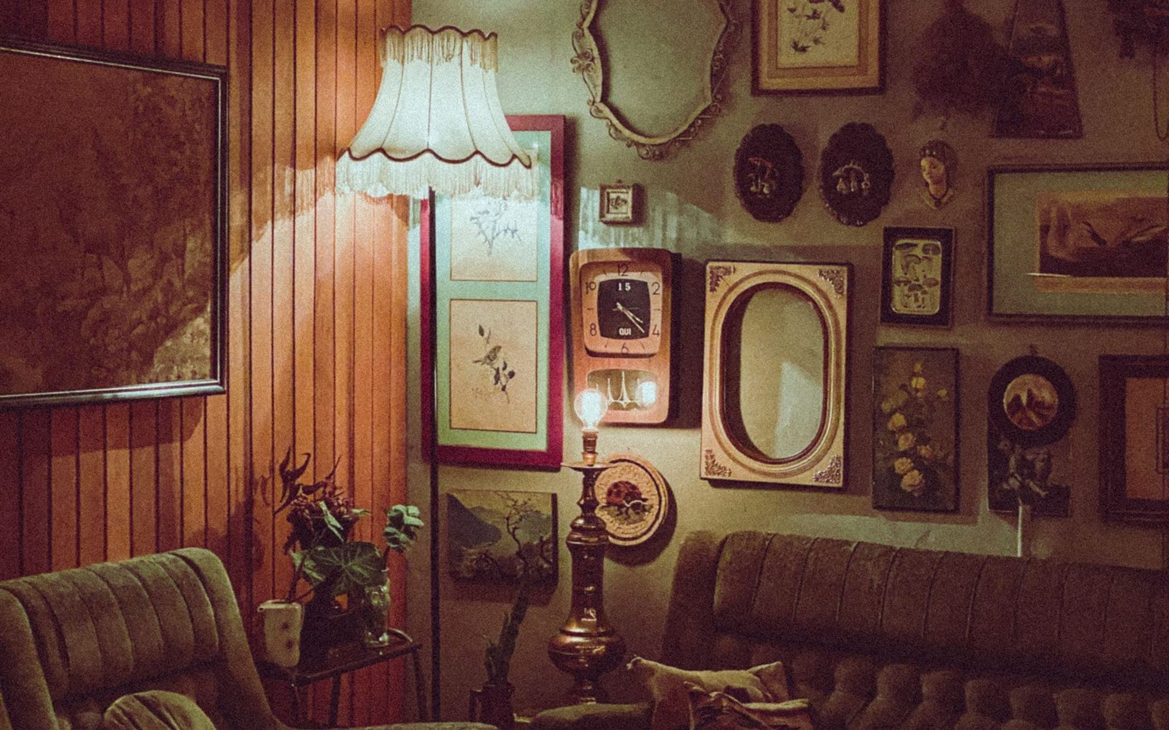 A dim vintage living room with a clock among framed pictures on the wall